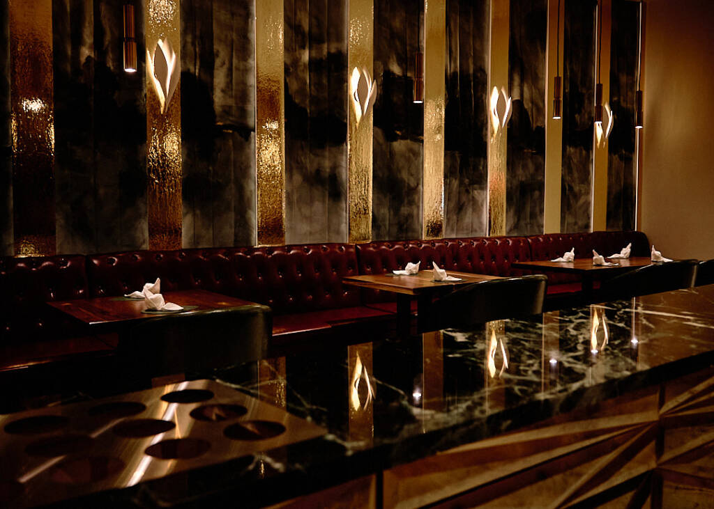 restaurant view with square table and a red couch against black and gold wall