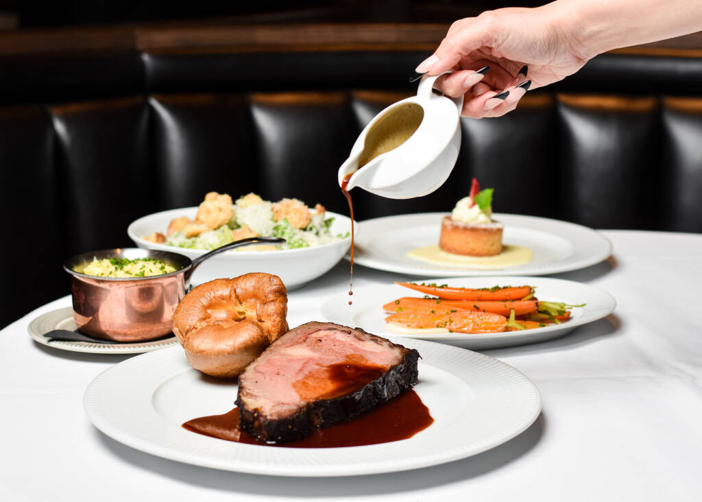 assortment of dishes, meat, carrots, desert and a hand pouring a sauce on a piece of meat