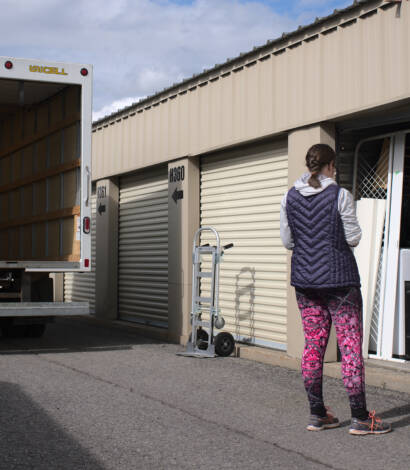 woman standing in front of storage locker and with moving truck in the back