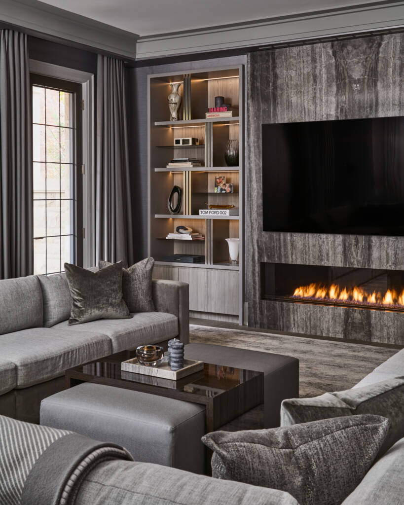 Living room with grey couches and coffee table, wall mounted tv, fireplace and bookshelf