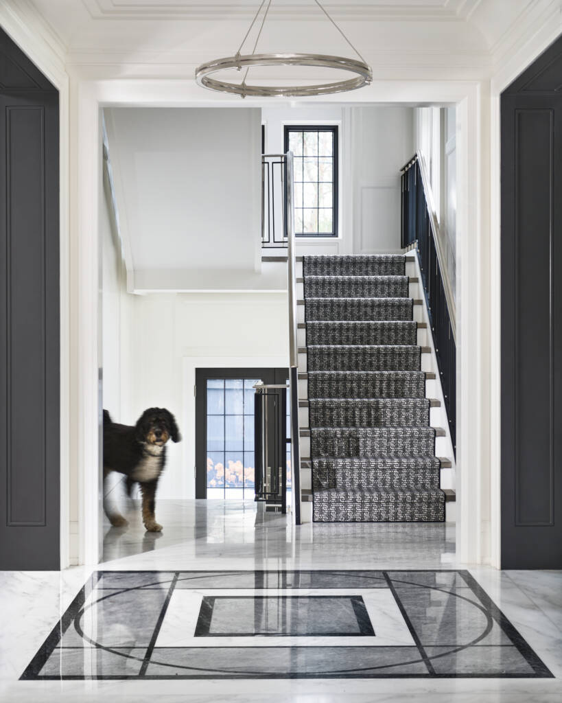 entry hall with black marble stair, patterned marble floor, gold pendant light, a black and white dog walking 